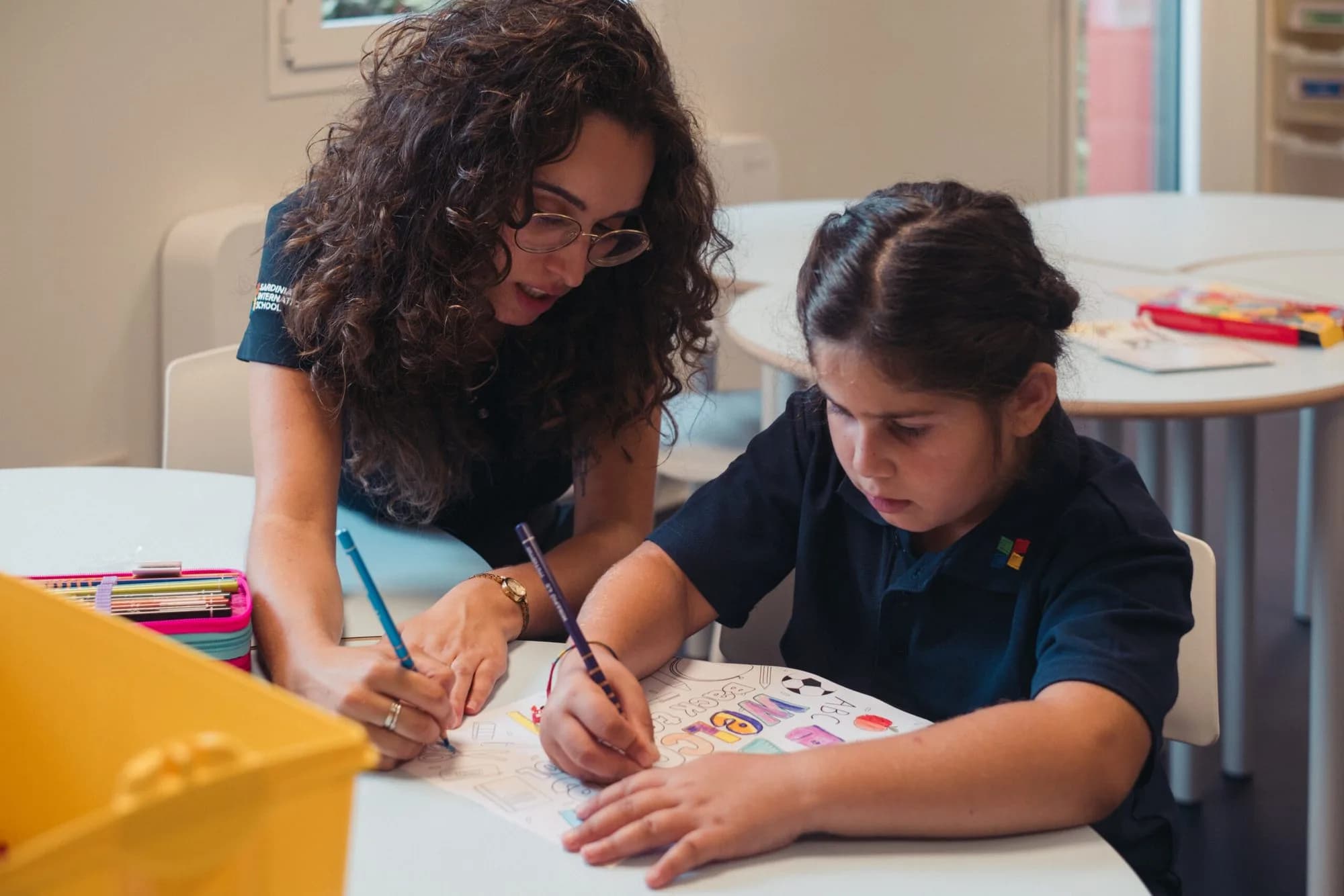 A teacher helping a young pupil with her drawing